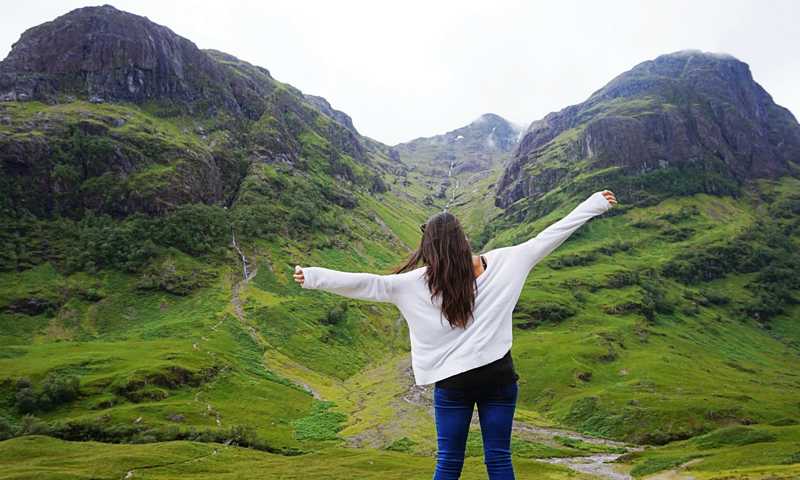Young woman with arms outstretched taking in the dramatic mountains and valleys of Glen Coe