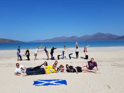 HAGGiS Adventures tour group forming letters with their bodies on the sunny Isle of Harris beach