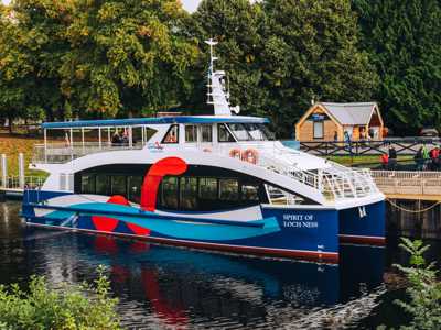 Loch Ness boat cruise docked at Fort Augustus harbour with calm waters reflecting summer skies