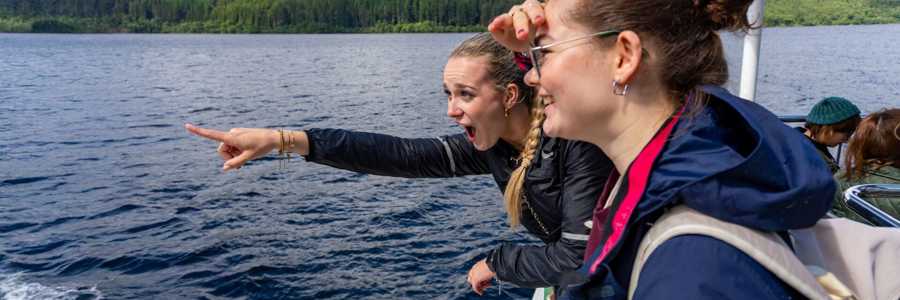 Two young women on a Loch Ness cruise leaning over the railing eagerly searching for Nessie