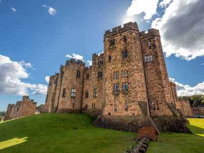 Alnwick Castle exterior basking in sunlight, surrounded by lush green grass and medieval charm