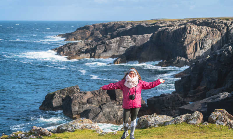 Young woman standing before the rugged coast on a sunny day in the Outer Hebrides