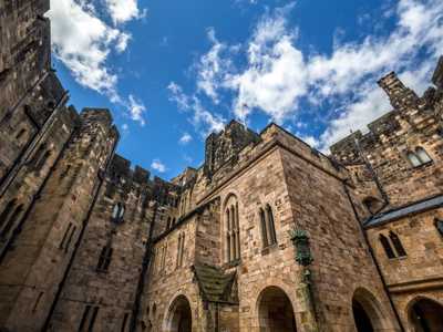 pward view of Alnwick Castle’s imposing stone walls against a bright blue sky from the courtyard
