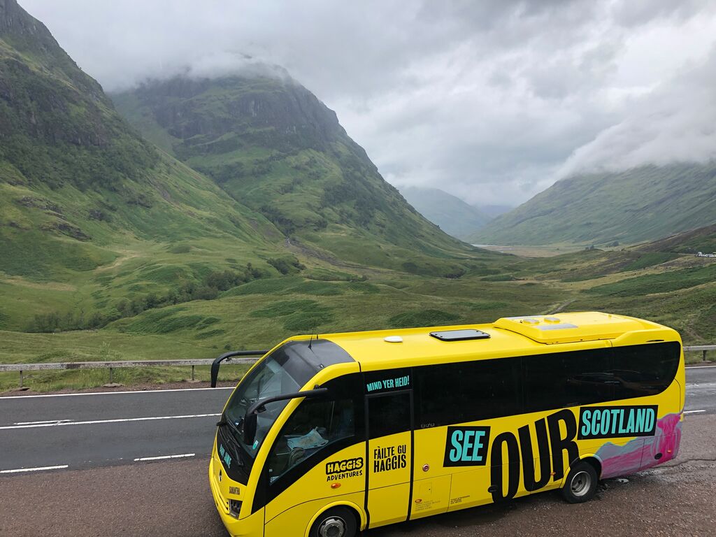 Yellow Haggis Adventures bus at Glen Coe valley with green hills in the background