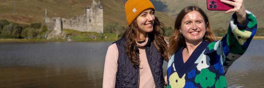 Two female travellers taking a selfie in front of Kilchurn Castle