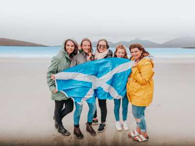 Group of young women holding a Scottish flag on the white sandy beach of the Isle of Harris