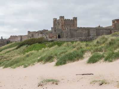 View of Bamburgh Castle rising above golden sandy beach with waves lapping at the shore