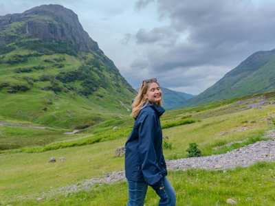 Smiling young woman walking through a valley with Glen Coe in the backround